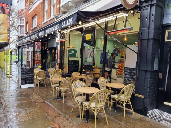 Street-level view of the green shopfront with outdoor seating along the pavement