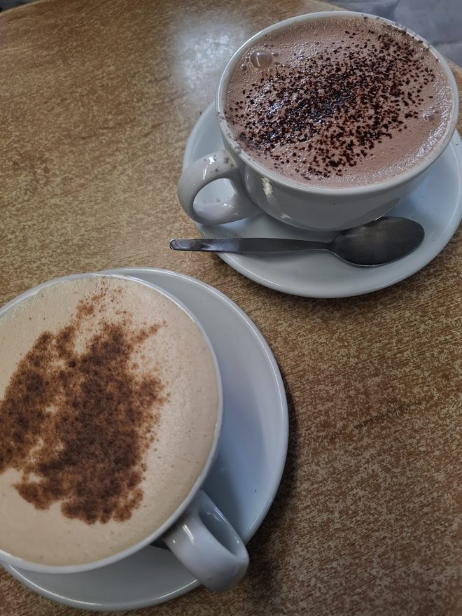 Two cappuccinos side by side on a wooden table